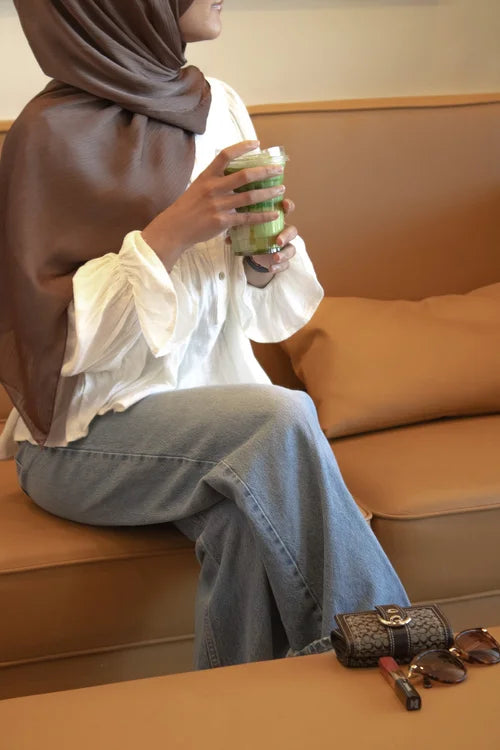 Woman in a mocha hijab relaxing on a sofa with a matcha drink